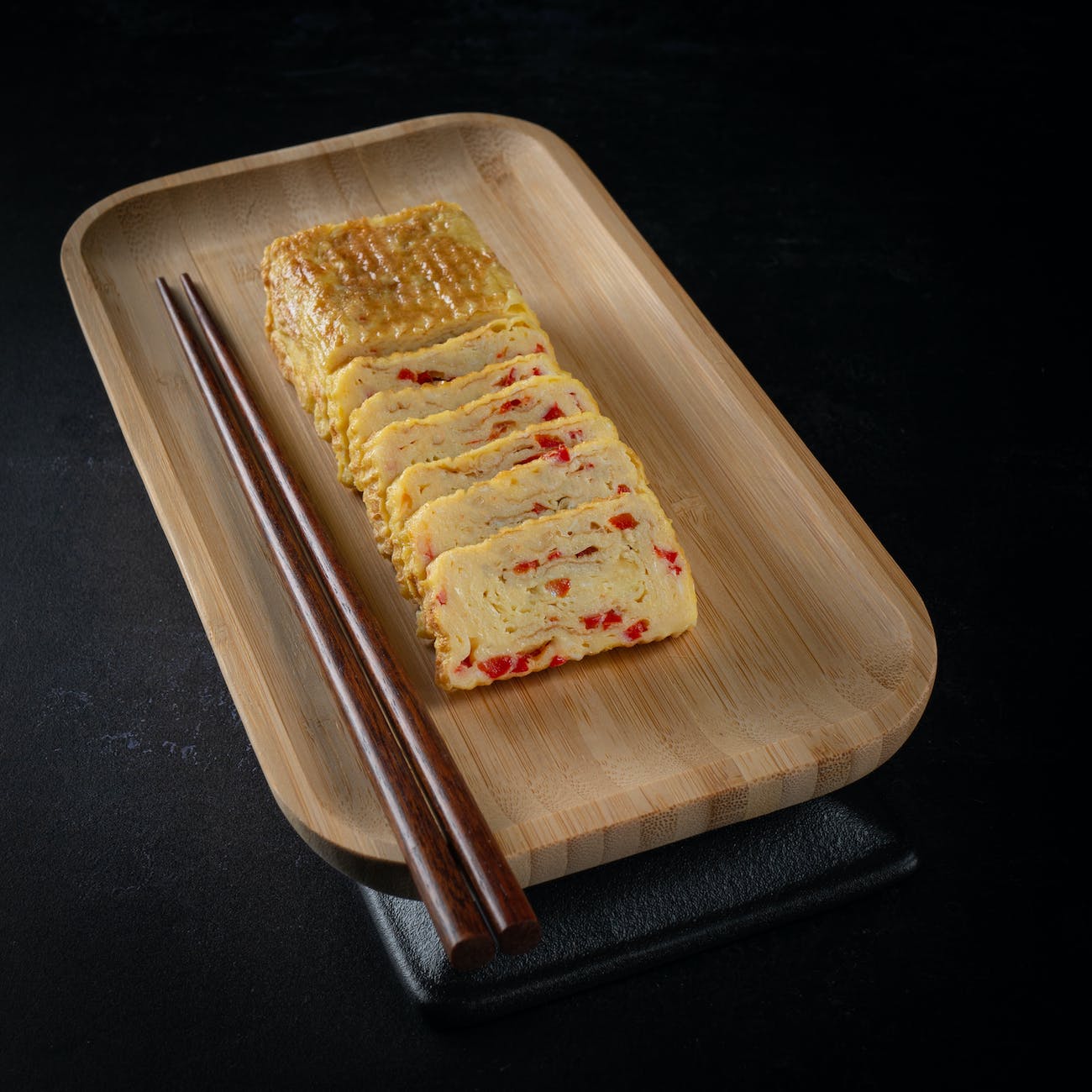 tamagoyaki omelett mit stäbchen auf langem viereckigen bambusteller